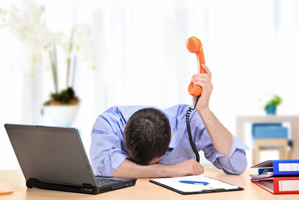 An exhausted businessman holding a telephone while conducting a telephone interview from his office