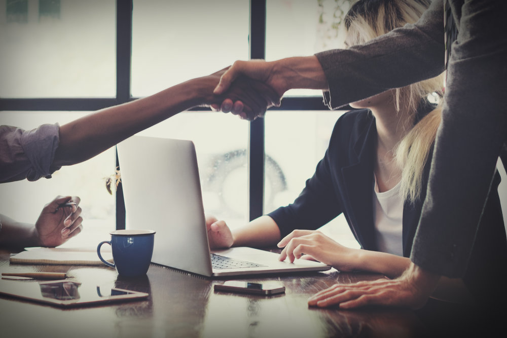 Two people shaking hands at the end of a structured interview while someone takes notes on a laptop.